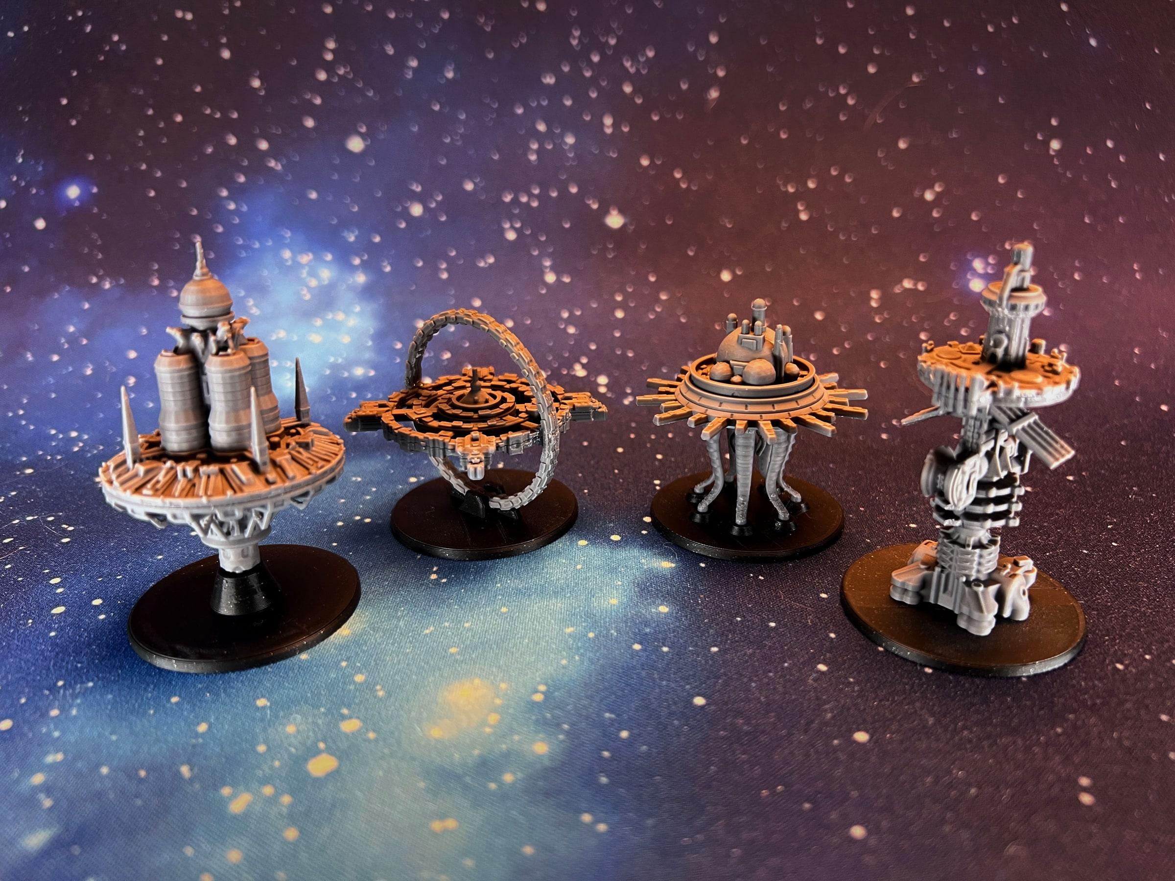 Four printed Twilight Imperium space-station miniatures on round stands, against a starfield.