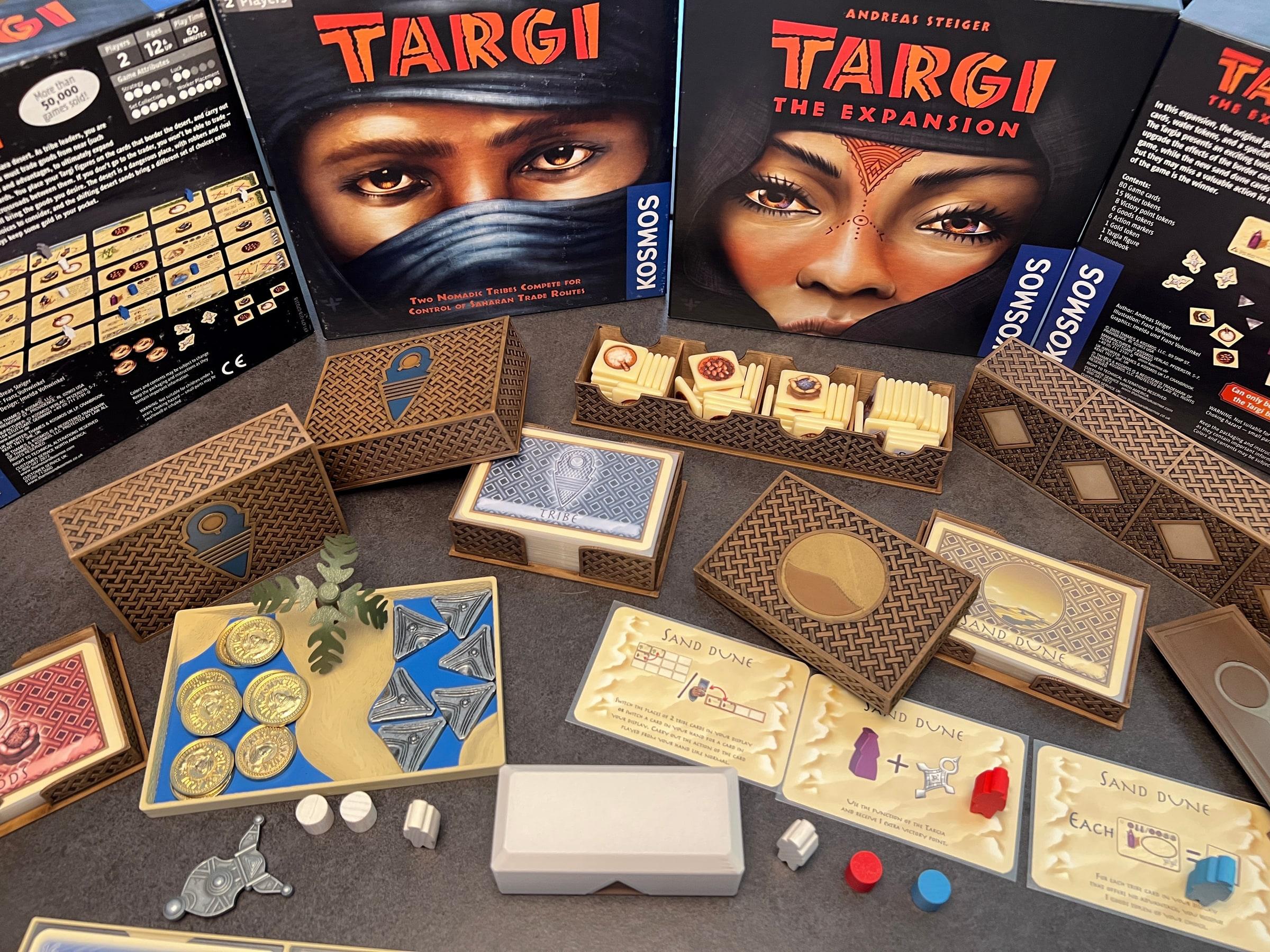 The Targi insert collection in front of the base game and expansion boxes: woven-pattern card boxes, a token rack and an oasis tray holding coins.